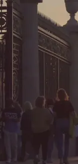 People walking past ornate gate at sunset.