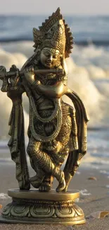 Golden Krishna statue on a beach with ocean waves in the background.