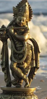 Golden Krishna statue on tranquil beach with ocean waves.