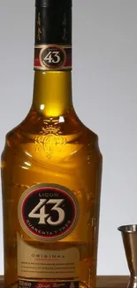 Golden liquor bottle with jigger on wooden surface.