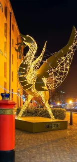 Illuminated golden sculpture at night with urban backdrop and street lights.