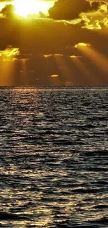 Golden sunset over a calm ocean with sun rays breaking through clouds.