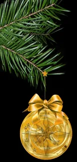 Golden ornament hanging from pine branch on black background.