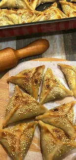 Golden brown triangular pastries topped with sesame seeds on a wooden board.