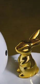 Golden rabbit statue beside white polka dotted egg on a plate.