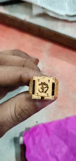 A gold ring with a Hindu symbol held in hand against a colorful background.