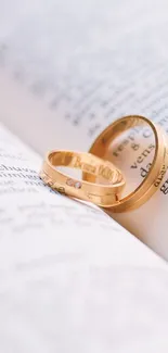 Golden rings resting on open book pages for a romantic mobile wallpaper.