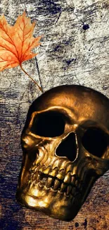 Golden skull with autumn leaf on textured dark background.