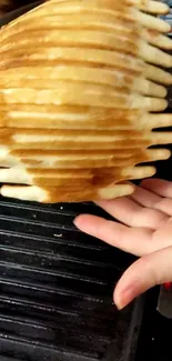 Golden brown pancake stack on a grill with hand.