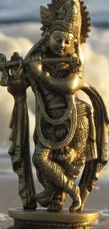 Golden statue of Lord Krishna playing the flute on a beach.