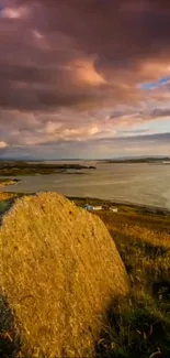 Golden sunset over a scenic coastal landscape with a large rock in the foreground.