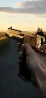 Hand holding a golden gun against a scenic sunset backdrop.