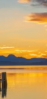 Golden sunset over a calm lake with silhouettes of mountains.