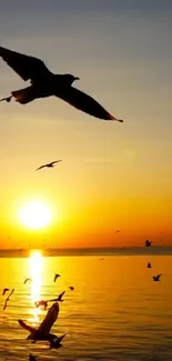 Mobile wallpaper of birds flying over the ocean at golden sunset.