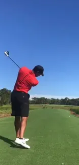 Golfer swings on a clear day against a vibrant blue sky and green fairway.