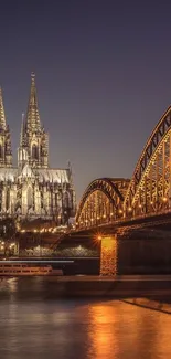 Gothic cathedral under night sky with illuminated bridge and reflections.