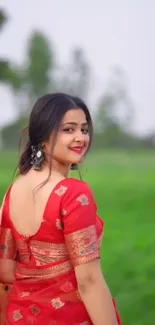 Woman in a red saree against a green field backdrop.