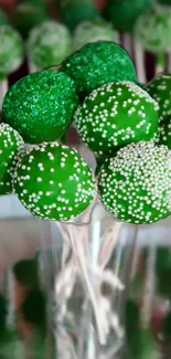 Green cake pops decorated with white sprinkles in a glass.