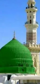 Green dome and minaret under clear blue sky background.