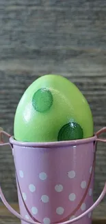 Green egg in pink polka dotted bucket on wooden background.