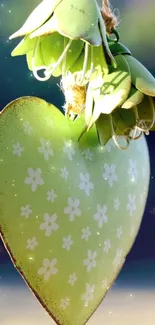 Green heart with floral pattern and leafy top against a serene background.