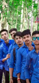 Group of friends in blue shirts posing in a lush, green forest setting.