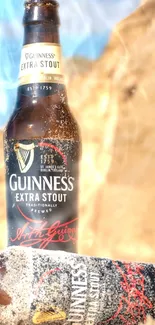 Guinness Extra Stout bottle on sandy beach under sun.