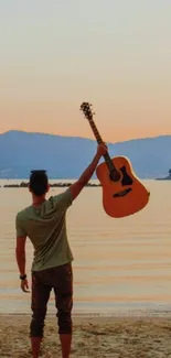 Person holding a guitar at a beach during sunset, creating a serene scene.