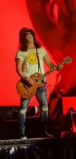 Guitarist performing on stage with a vivid red backdrop.