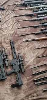 Collection of guns on a brown blanket, including rifles and shotguns.