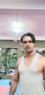 Man in gym wearing gray tank top with gym equipment in background.