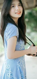 Young woman in blue dress holding a camera outdoors.