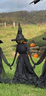 Three witches in black dresses with pumpkins and a scenic autumn backdrop.