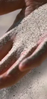 A hand gently holding beige sand grains.