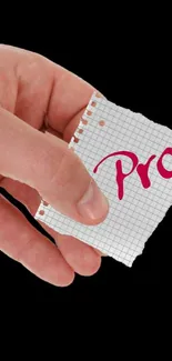 Hand holding a grid paper note with 'Pro' on black wallpaper.