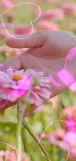 Hand holding a pink flower with heart overlays in a meadow.