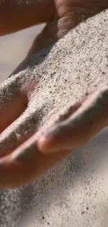 A close-up of a hand letting sand flow gently through fingers on a mobile wallpaper.