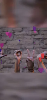 Hands making gestures with colorful heart symbols on a brick wall.