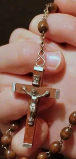 Hands holding a cross-styled rosary in prayer.