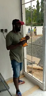 Construction worker with drill by a window amid building site.