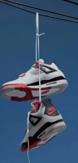 Sneakers hang from a wire against a blue sky.