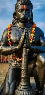 Hanuman statue in prayer pose with mace and garland.