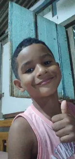 Child smiling in a rustic room with a thumbs-up gesture.