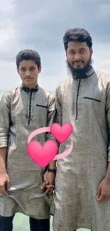 Two friends in traditional attire by the sea with heart graphics.