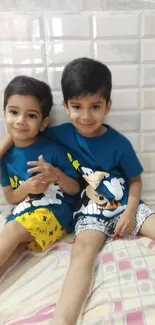 Two young boys in blue cartoon shirts sitting happily together.