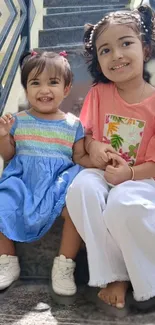 Two smiling children sitting on stairs in casual outfits.