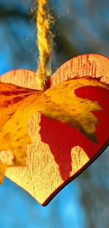 Heart and autumn leaf hanging against a blue sky.