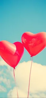 Two red heart-shaped balloons against a clear blue sky.