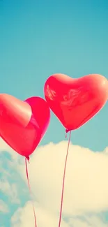 Two red heart balloons float in a blue sky with clouds.