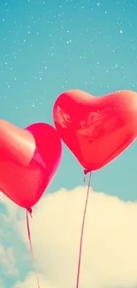 Two red heart balloons floating in a blue sky with clouds.